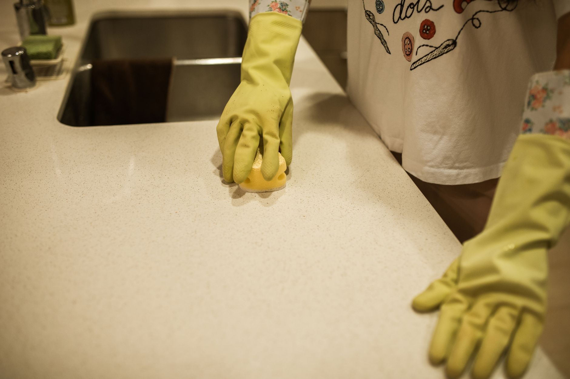 Gloved hand cleaning a kitchen counter with a sponge